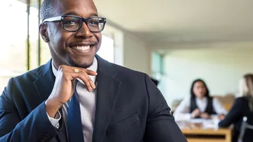 Person in a suit smiling in an office setting.