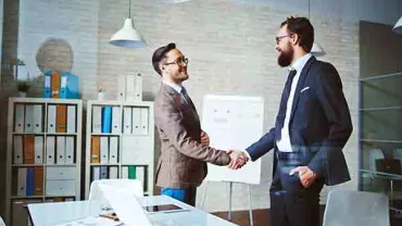 Two people shaking hands in a modern office setting.