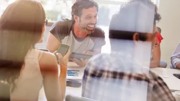 People having a friendly meeting in an office, smiling and using devices.