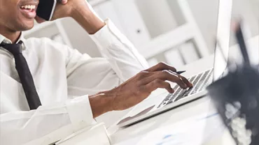 Person on phone using a laptop at a desk.