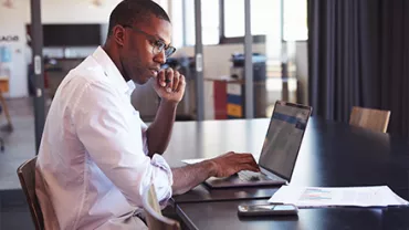 Person working on a laptop at a table with documents.