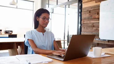 Person working on a laptop at a wooden desk in a modern office.