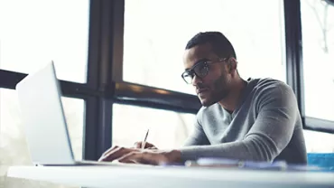 Person working on a laptop at a desk by a large window.