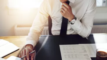 Person in formal attire working on a laptop with documents on the desk.