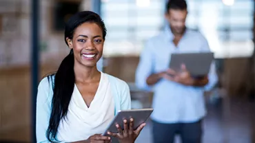 Person smiling while using a tablet, blurred office setting.