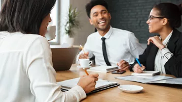 Three people smiling and talking during a meeting in an office setting.