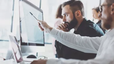 People working together at a computer, analyzing data on a screen.