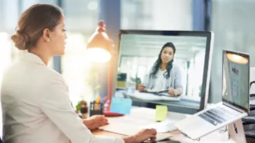 Person using a computer to video call a colleague in a bright office.